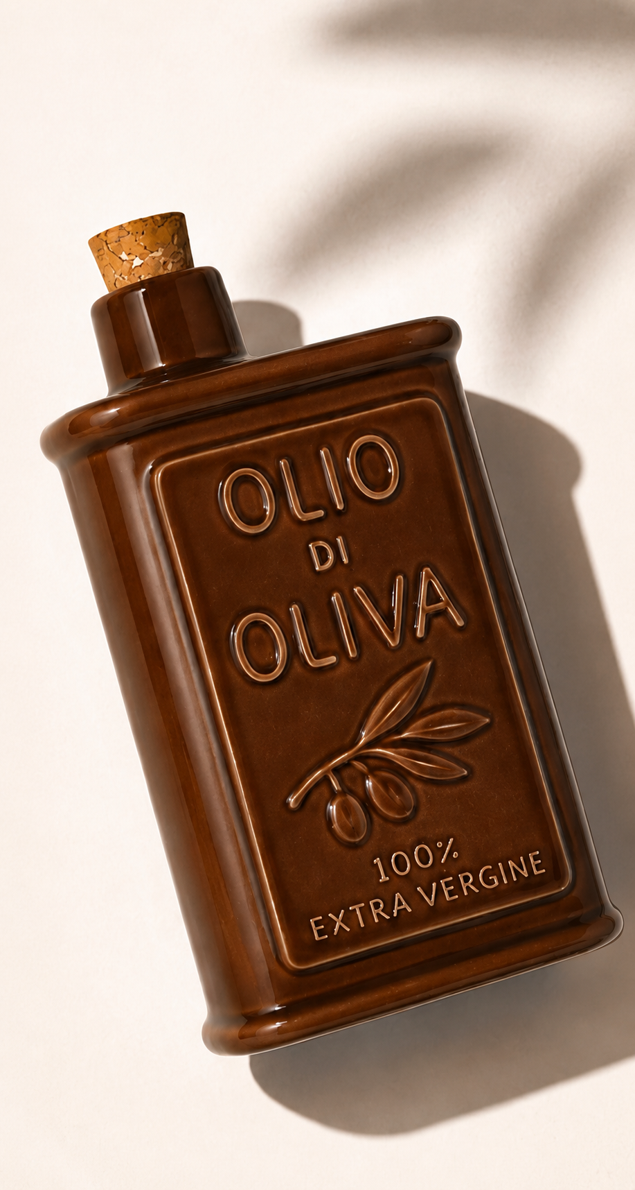 A dark brown embossed glass bottle of olive oil with a cork stopper, featuring embossed text reading 'OLIO DI OLIVA' and '100% EXTRA VERGINE' on a warm off-white background with soft leaf shadows.
Details