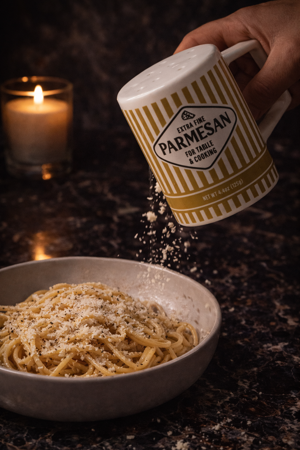 Person sprinkling Parmesan cheese from a striped container onto spaghetti.