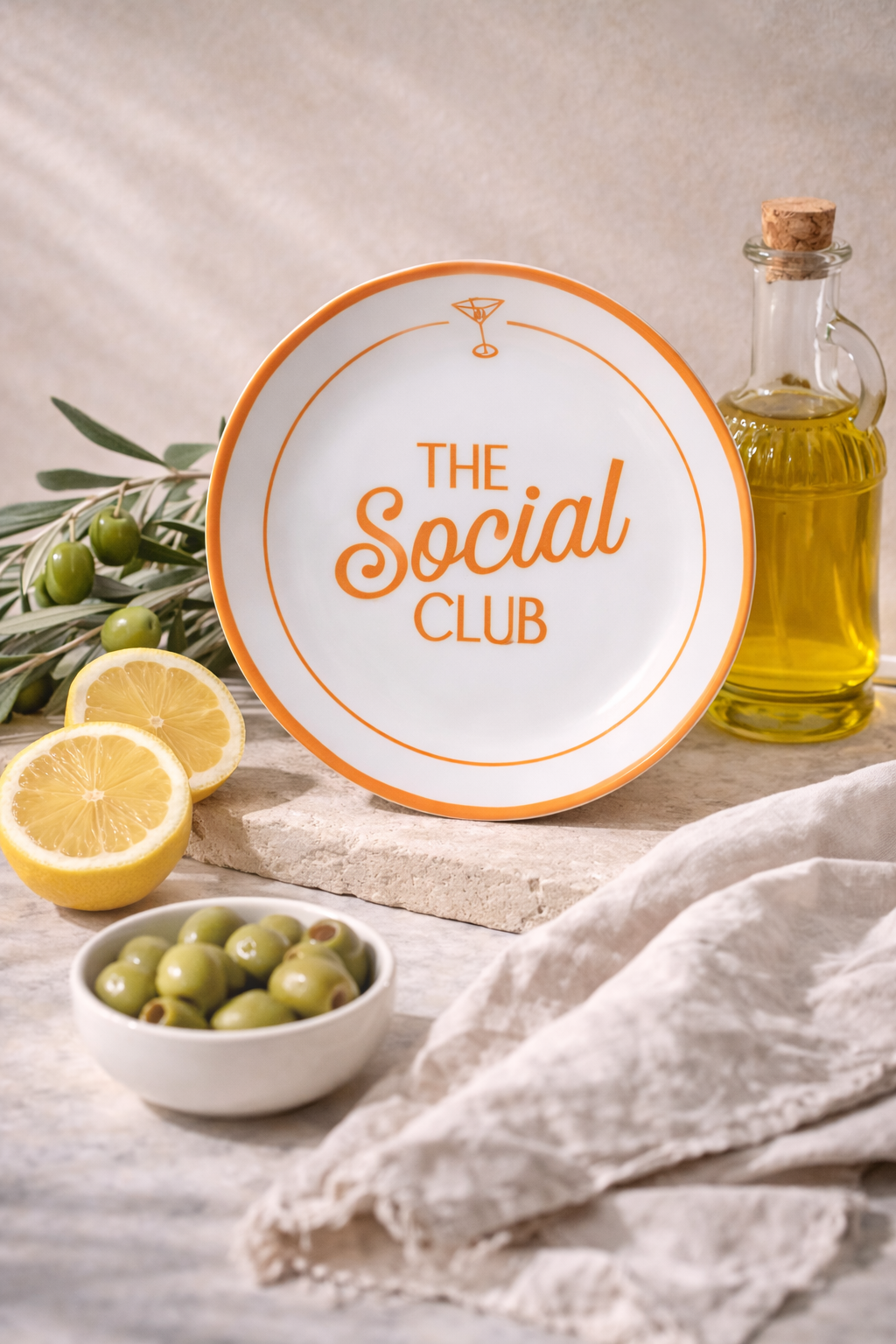 Decorative side plate with 'The Social Club' text, lemons, olives, and a bottle of oil on a wooden surface. Italian dinnerware for aperitivo hour.